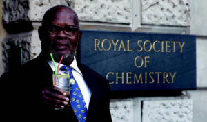 Photograph of Erasto Mpemba standing before the Royal Society of Chemistry.